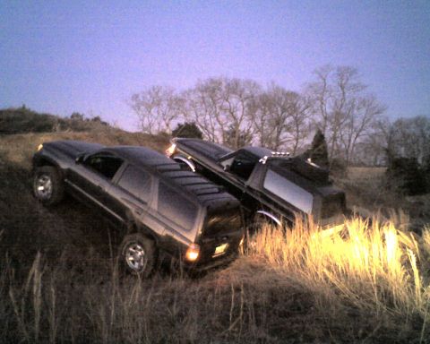 1995 Ford Bronco - Two SUVs are positioned on a grassy, uneven terrain under a twilight sky.