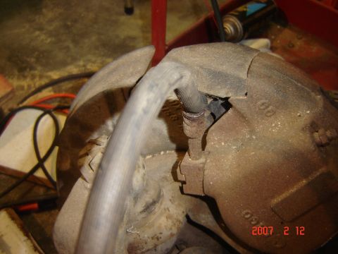 1993 Ford Bronco - A close-up view of a corroded vehicle brake caliper and its attached hose, with visible markings on the metal housing.