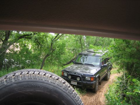 1996 Ford Bronco - A Land Rover Discovery navigates a wooded trail, with a spare tire visible in the foreground.