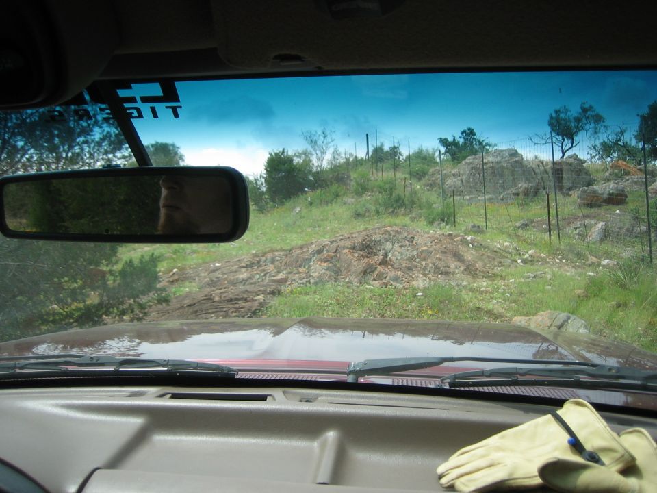 1996 Ford Bronco interior view, tan dashboard, windshield, rearview mirror showing driver's face, off-road landscape visible