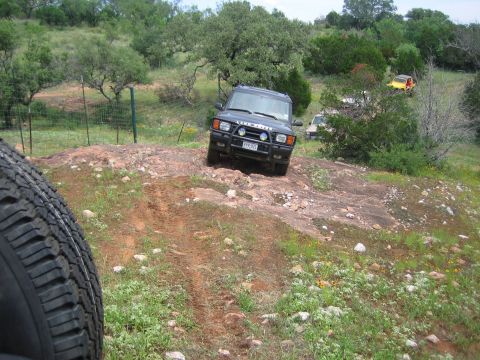 1996 Ford Bronco - A Land Rover Discovery tackles a challenging rocky path, with other vehicles visible further back.