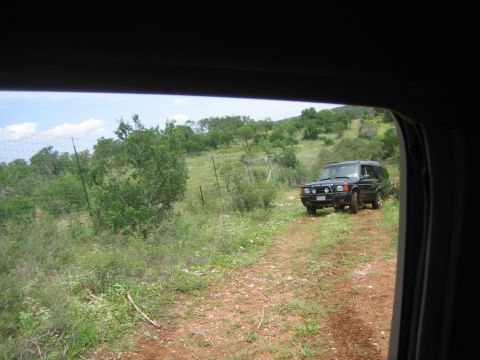 1996 Ford Bronco - A black Land Rover Discovery is parked on a dirt road surrounded by vegetation and hills.