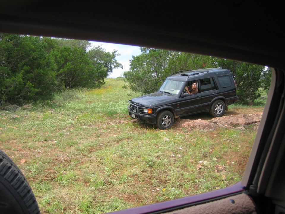 Black Land Rover Discovery SUV parked on a dirt path with green trees and grass