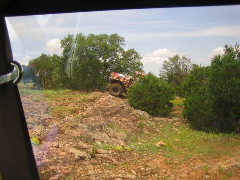 1996 Ford Bronco - An all-terrain vehicle navigates a rocky, wooded landscape under a partly cloudy sky.