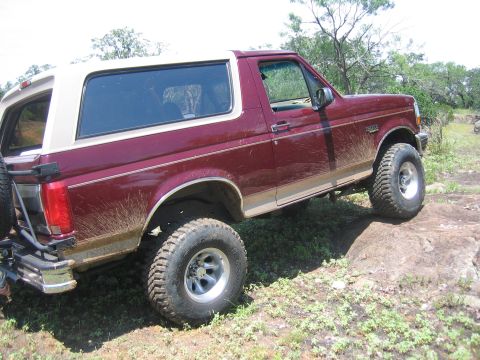 1996 Ford Bronco - 1996 Ford Bronco navigating a rocky trail with mud splattered on its body.