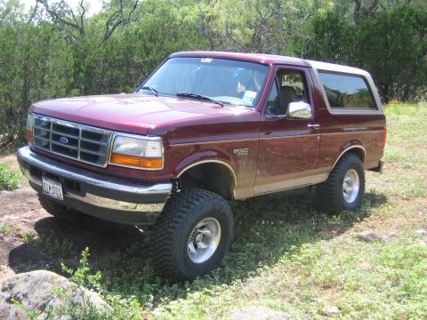 1996 Ford Bronco - This maroon Ford Bronco, likely from the early to mid-1990s, is shown with a lifted suspension and off-road tires.
