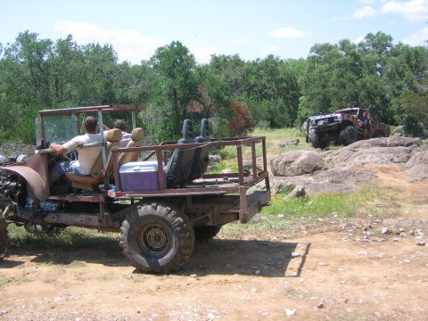 1996 Ford Bronco - Two custom off-road vehicles navigate a rocky, outdoor terrain on a sunny day.