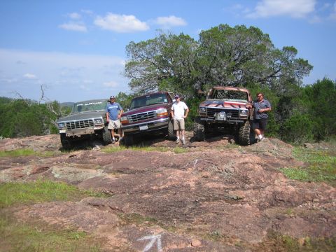 1996 Ford Bronco - Three men pose with their off-road trucks on a rocky landscape under a clear blue sky.
