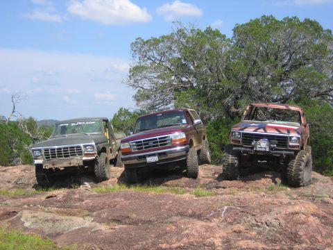 1996 Ford Bronco - A maroon 1996 Ford Bronco is parked on rocky terrain alongside two other off-road vehicles under a partly cloudy sky.