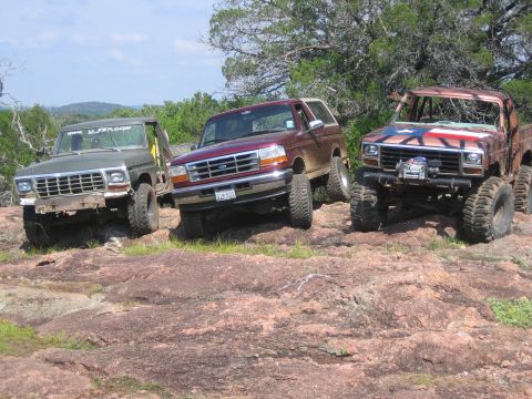 1996 Ford Bronco - Three modified SUVs, including a 1996 Ford Bronco, are parked on a rocky terrain.