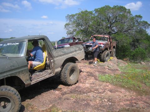 1996 Ford Bronco - Multiple off-road trucks navigate a challenging rocky terrain under a bright, partly cloudy sky.