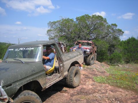 1996 Ford Bronco - Two mud-splattered Ford Broncos are parked on a rocky hill under a blue sky with scattered clouds.