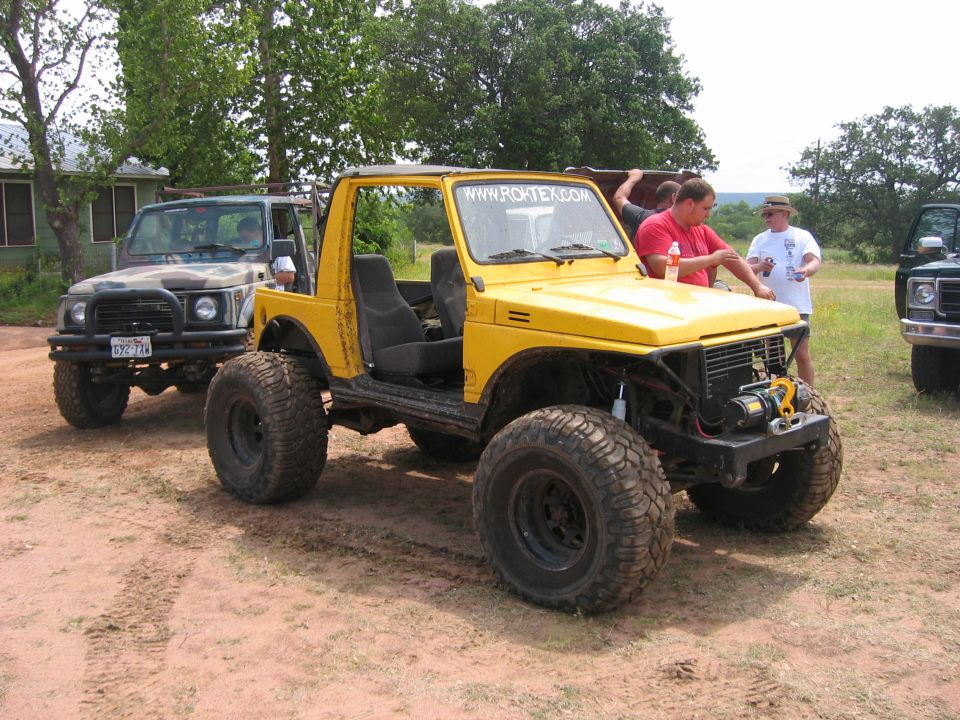 Yellow off-road vehicle with large tires and a winch, parked on dirt. Website www.roktex.com visible on windshield