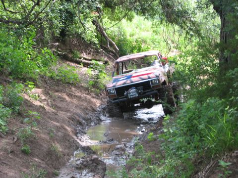 1996 Ford Bronco - This vehicle is navigating a challenging muddy trail surrounded by dense foliage.