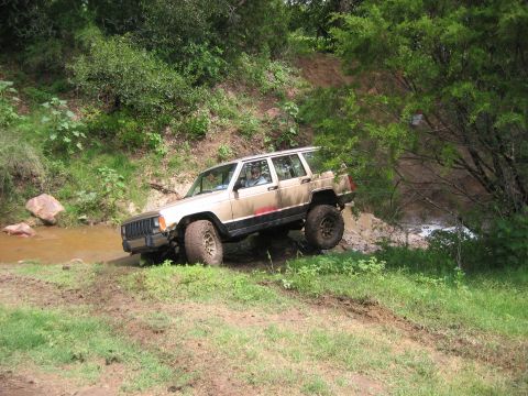 1996 Ford Bronco - Jeep Cherokee XJ navigates a challenging off-road course with mud and water obstacles.