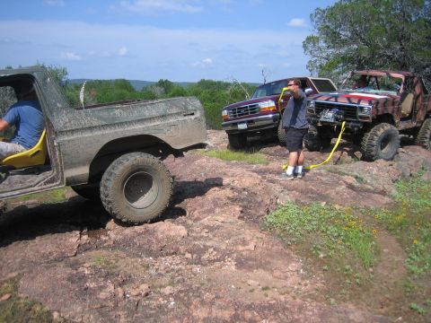 1996 Ford Bronco - A group of off-road vehicles navigate a challenging rocky trail under a bright blue sky.