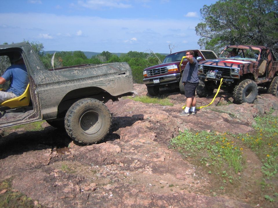 Three off-road vehicles on a rocky hill, one being winched