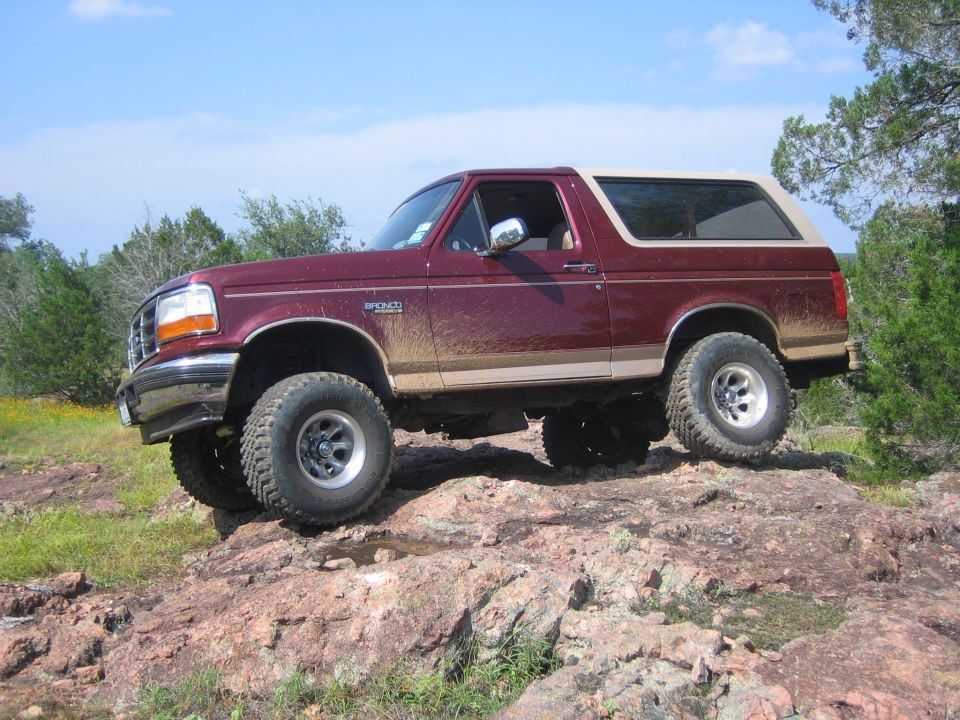 Maroon 1996 Ford Bronco with tan top, lifted on off-road tires, driving over rocks