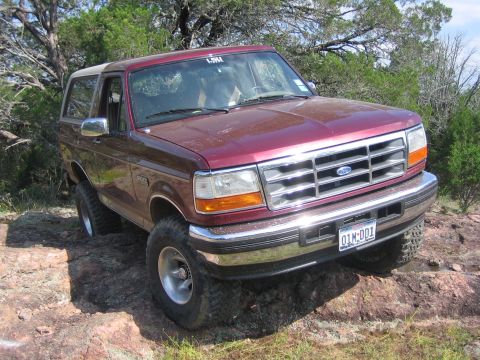 1996 Ford Bronco - This Ford Bronco is navigating a rocky terrain with trees in the background.