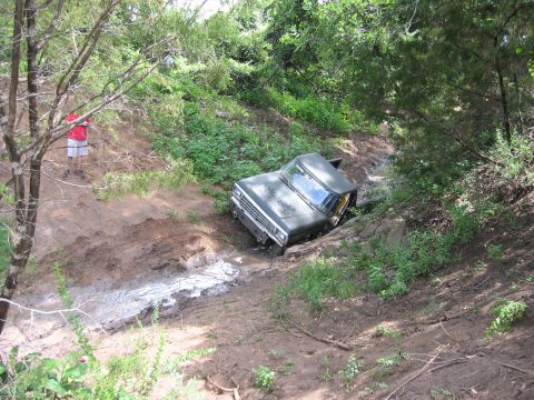 1996 Ford Bronco - A vintage Ford truck is stuck in a muddy ravine surrounded by trees and vegetation.