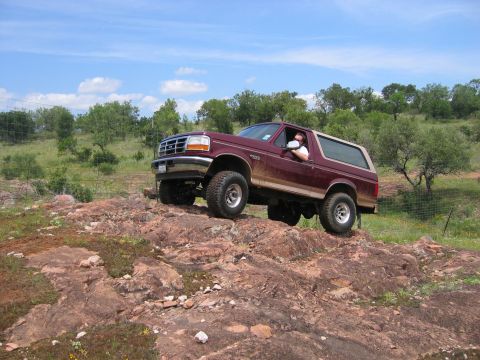 1996 Ford Bronco - A maroon 1996 Ford Bronco navigates a rocky trail under a blue sky with scattered clouds.