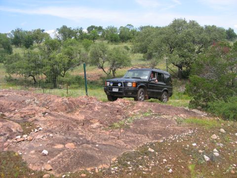 1996 Ford Bronco - Land Rover Discovery Series II navigates a rocky, off-road path under a partly cloudy sky.