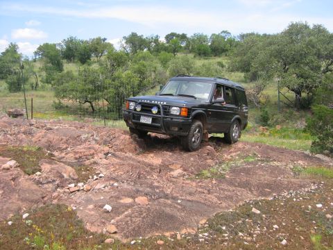 1996 Ford Bronco - A black Land Rover Discovery navigates a rocky terrain under a partly cloudy sky.