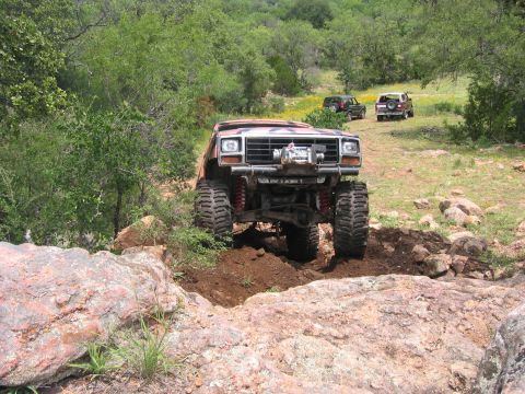 1996 Ford Bronco - This heavily modified truck, likely from the 1980s, tackles a challenging off-road course with two other vehicles in the background.