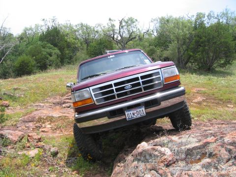 1996 Ford Bronco - 1996 Ford Bronco navigating a rocky trail in a wooded area.