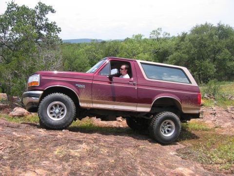 1996 Ford Bronco - This Ford Bronco is shown off-road, navigating a rocky path with trees in the background.