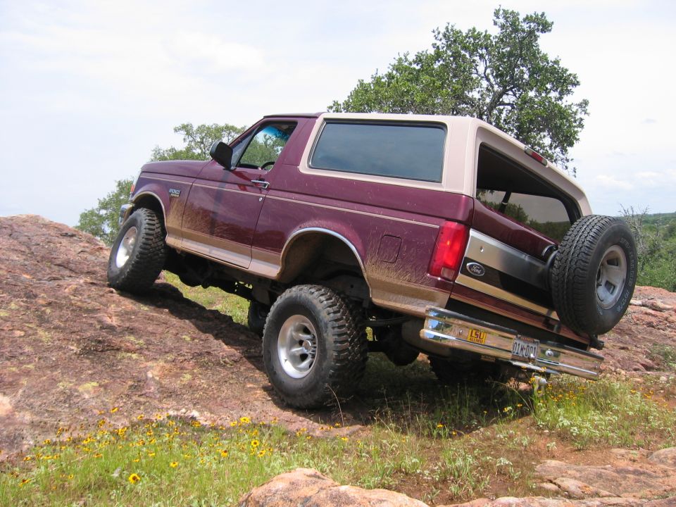 Maroon Ford Bronco with tan top climbing a rocky incline, spare tire mounted on rear