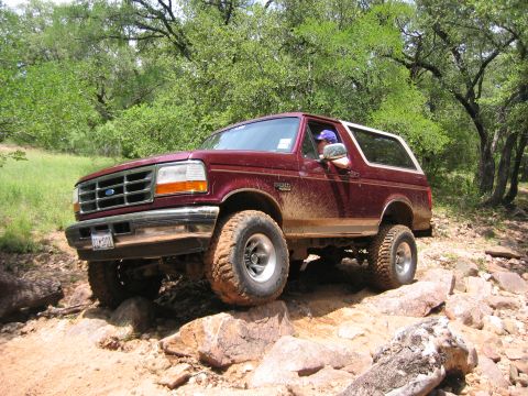 1996 Ford Bronco - A maroon Ford Bronco navigates a rocky trail, its tires covered in mud.