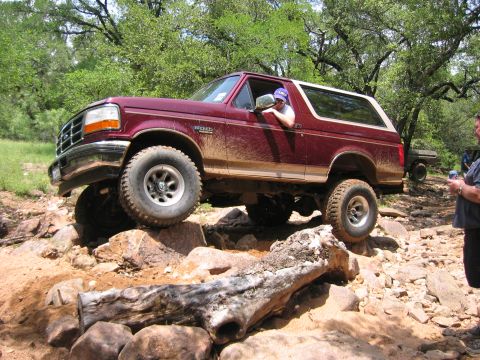 1996 Ford Bronco - A maroon 1996 Ford Bronco is shown navigating a challenging rocky trail with another vehicle visible in the background.
