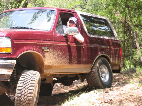 1996 Ford Bronco - 1996 Ford Bronco navigating a rough, off-road trail with mud splattered on its side.