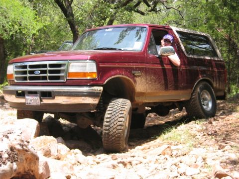 1996 Ford Bronco - A mud-splattered Ford Bronco navigates a challenging, rocky off-road path.