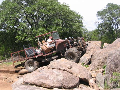 1996 Ford Bronco - A custom-built off-road vehicle is shown traversing a rocky terrain with trees in the background.