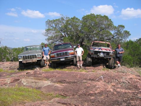 1996 Ford Bronco - Four men pose with three off-road vehicles on a rocky landscape under a blue sky.