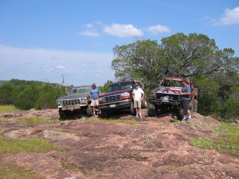 1996 Ford Bronco - Four off-road vehicles are parked on a rocky terrain under a clear blue sky with scattered clouds.