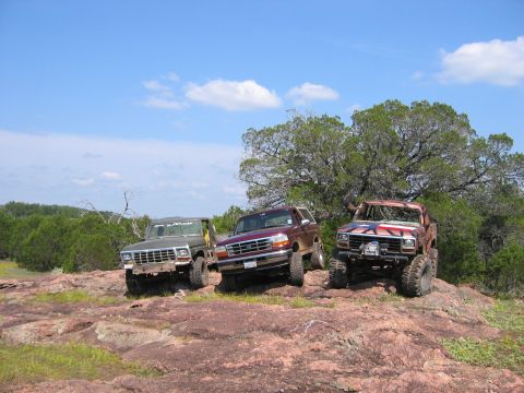 1996 Ford Bronco - Three Ford Broncos, one with a Texas flag motif, are parked on a rocky hill.