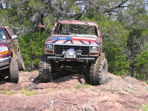 1996 Ford Bronco - Two off-road vehicles are parked on a rocky incline surrounded by trees.