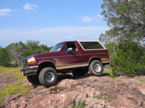 1996 Ford Bronco - A maroon 1996 Ford Bronco navigates a rocky trail under a blue sky.