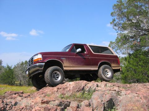 1996 Ford Bronco - A maroon 1996 Ford Bronco navigates a rocky terrain under a clear blue sky.