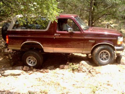 1996 Ford Bronco - This 1996 Ford Bronco is shown in a side profile, navigating a rocky, wooded terrain.