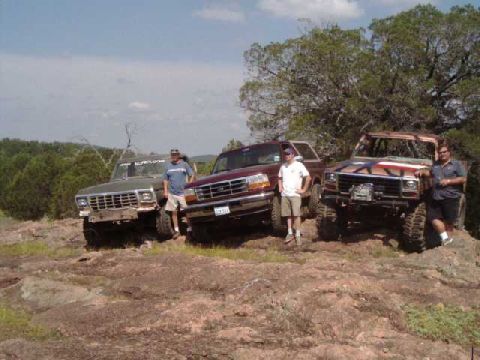 1996 Ford Bronco - Three off-road SUVs are parked on a rocky hill under a partly cloudy sky.