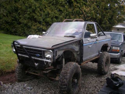 1984 Ford Bronco II - A modified Ford Bronco II sits in a gravel lot next to another vehicle, showing its lifted suspension and large tires.