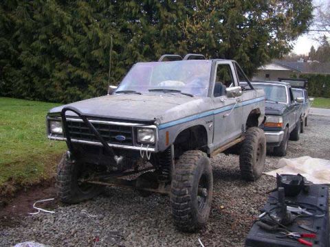 1984 Ford Bronco II - A lifted 1984 Ford Bronco II is parked in front of other vehicles on a gravel surface.
