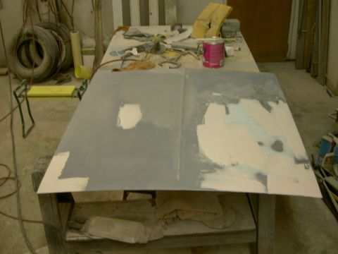 1967 Ford Ranchero - A car hood is being repaired with body filler and primer in a workshop setting.