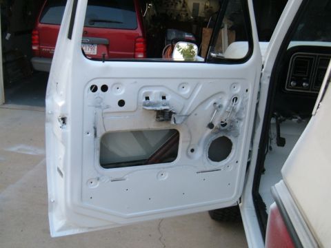 1978 Ford Bronco - The interior of a vehicle door is shown with the panel removed, revealing internal components. A red SUV is visible in the background.