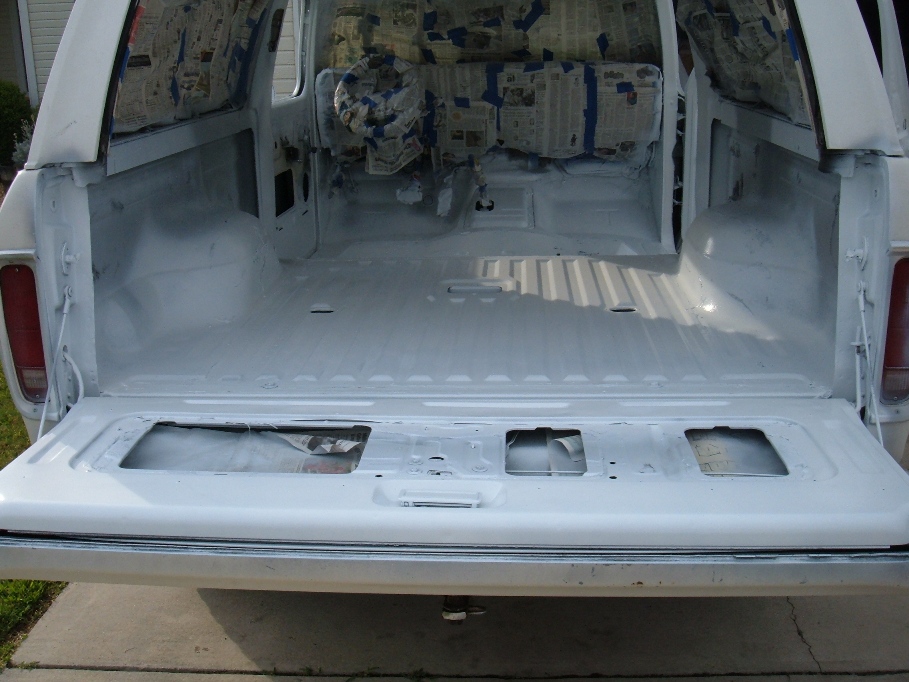 White SUV interior with seats covered in newspaper and tape, tailgate open, undergoing renovation