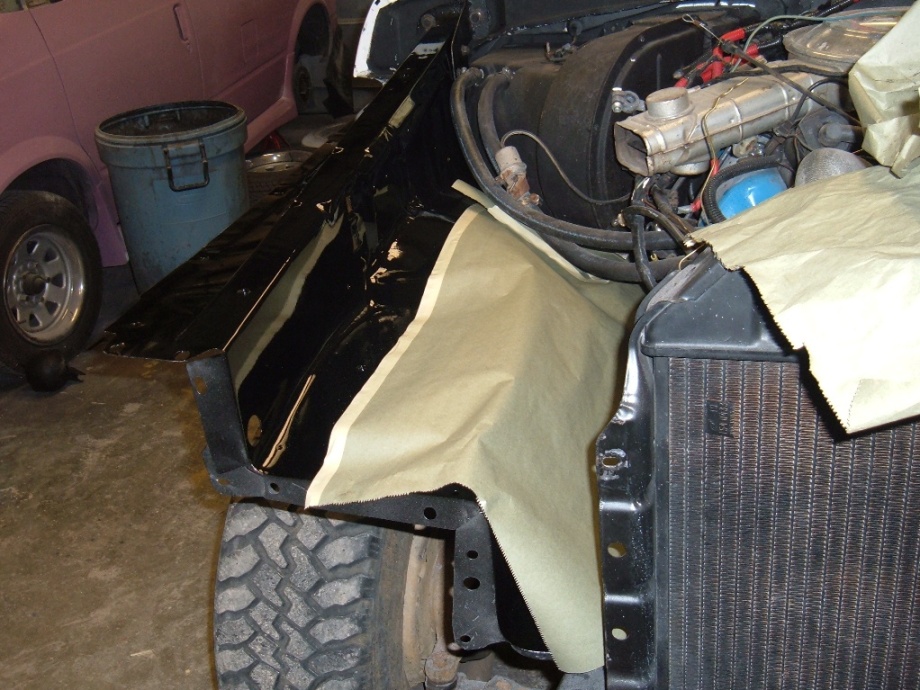Bronco with fender removed, freshly painted black inner fender masked with paper, engine and radiator exposed